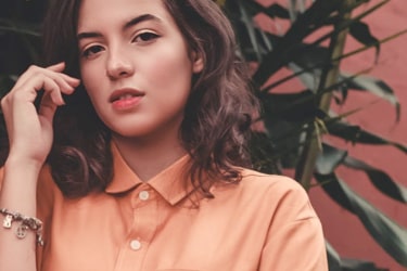 Female model with black hair on shoulders wearing orange shirt